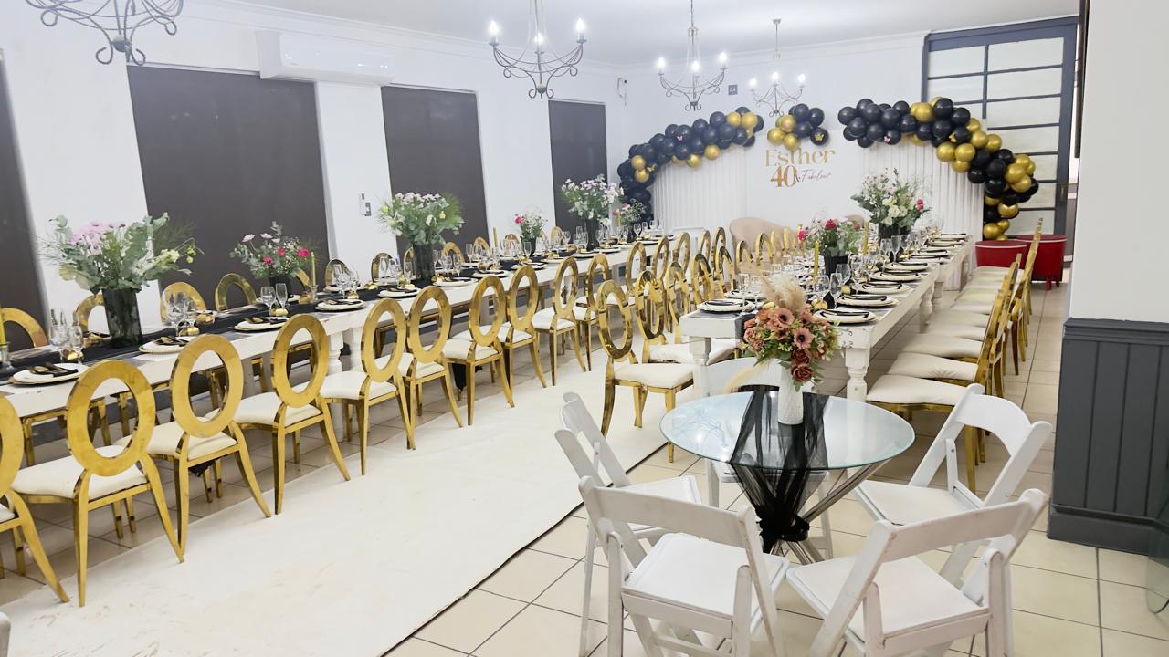 Gold and black birthday setup with a balloon arch and gold chairs