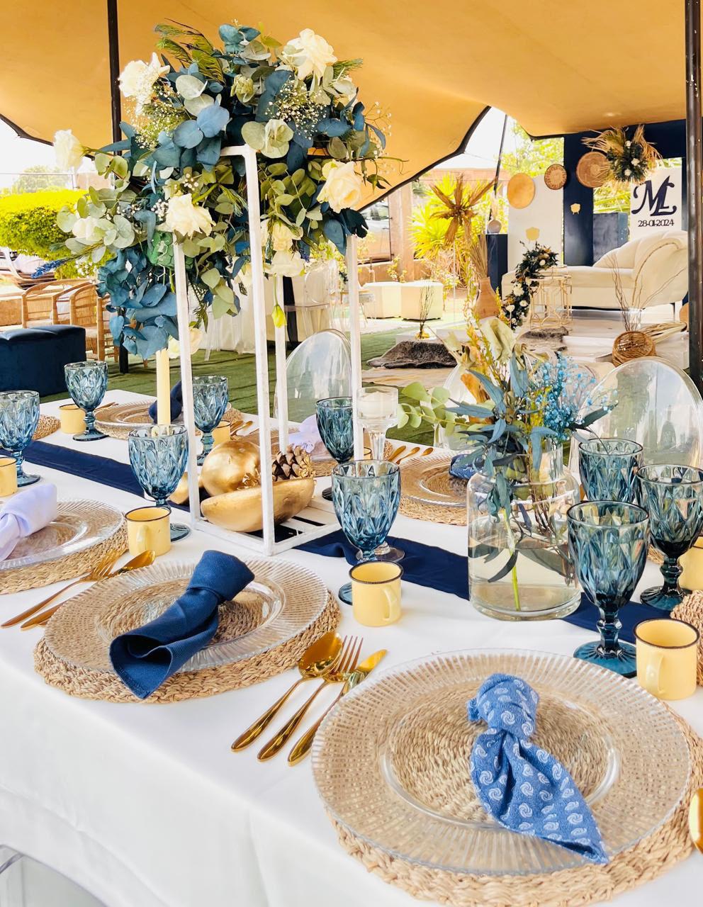 Blue and gold wedding table with floral centrepiece, glass goblets and woven placemats